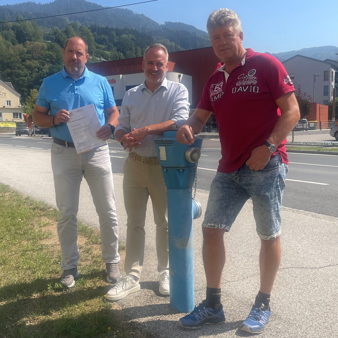 Drei Männer vor einem blauen Hydranten in einer bergigen Landschaft.
